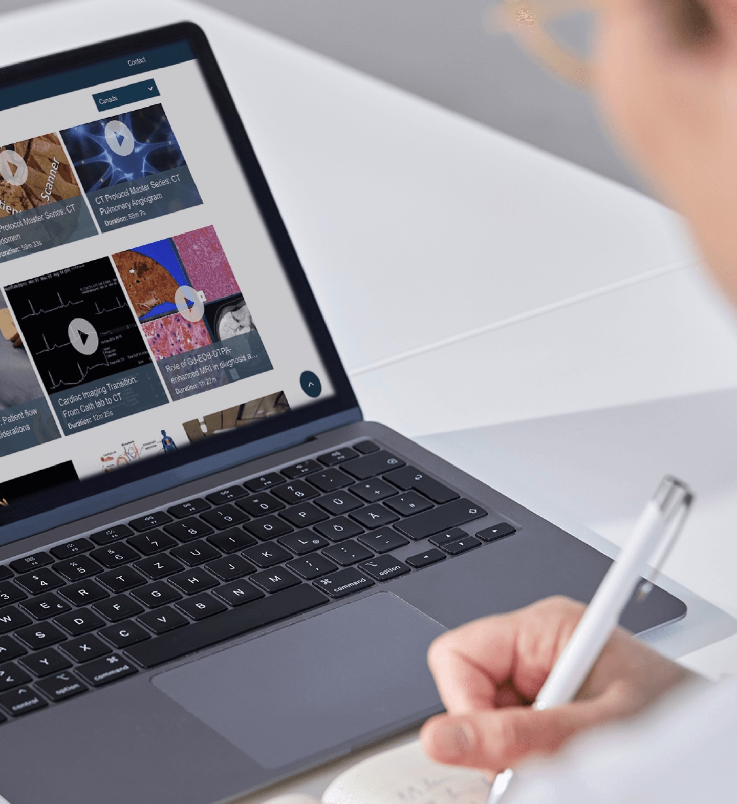 Laptop with video library and person writing in front of it